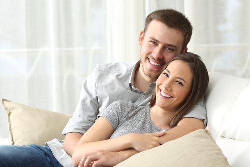 Husband and wife laughing while sitting on sofa. 