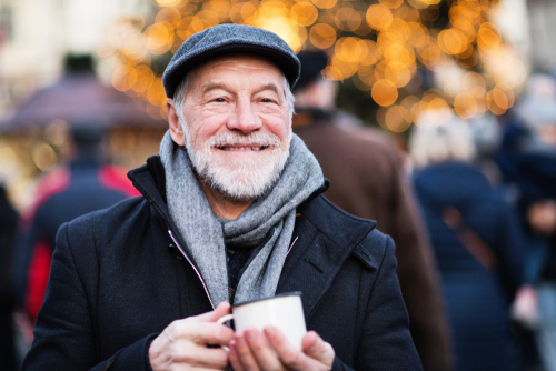 An elderly man smiling and holding a mug