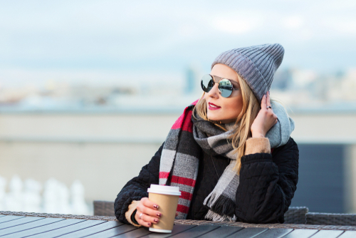 woman wearing winter clothing and sunglasses while holding a cup of coffee